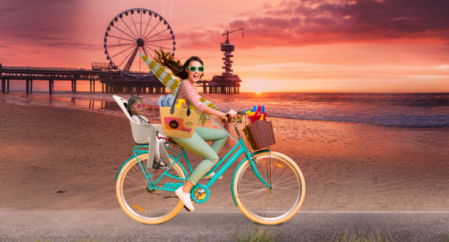 Fictief beeld van een vrouw op een fiets op het strand in Scheveningen en een kindje achterop Fictief beeld van een vrouw op een fiets op het strand in Scheveningen en een kindje achterop