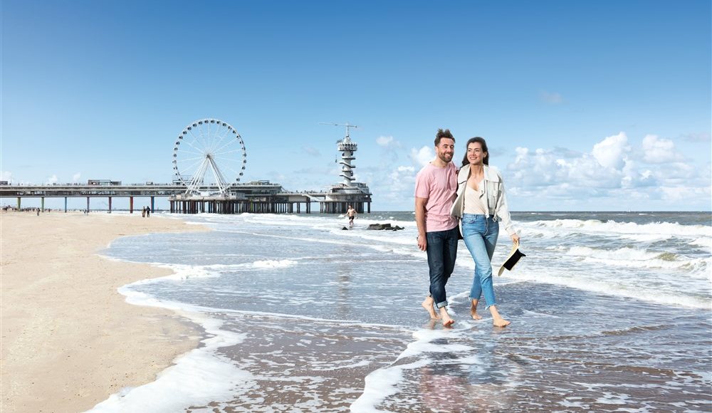 Koppel wandelt op strand Scheveningen met de Pier en het reuzenrad op de achtergrond Koppel wandelt op strand Scheveningen met de Pier en het reuzenrad op de achtergrond